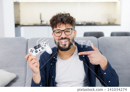 Happy man holding gaming controller pointing at it Happy man holding gaming controller pointing at it 141034274