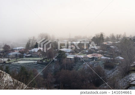 The image depicts dwellings with tiled roofs, enveloped in a dense mist The image depicts dwellings with tiled roofs, enveloped in a dense mist 141034661