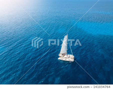Aerial drone view of sailing catamaran yacht moving in blue sea Aerial drone view of sailing catamaran yacht moving in blue sea 141034764