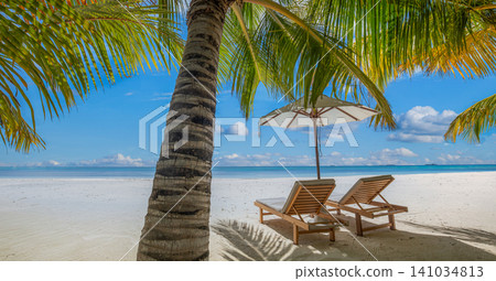 Beach beds beneath swaying palms on turquoise shore. Red parasol casting shade over white sand. Idyllic island resort for luxury travel summer holiday Beach beds beneath swaying palms on turquoise shore. Red parasol casting shade over white sand. Idyllic island resort for luxury travel summer holiday 141034813