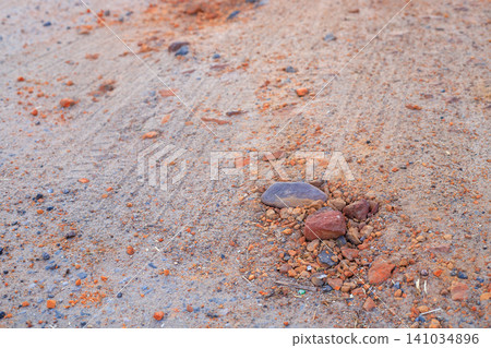 Small stones and fragments of orange clay are scattered across the dry, sandy surface of the road. Small stones and fragments of orange clay are scattered across the dry, sandy surface of the road. 141034896