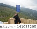Young woman posing with a blue prayer flag at a scenic tea garden viewpoint in Tinchuley Darjeeling 141035295