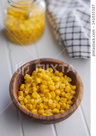 Bright Sweet Corn Kernels In A Wooden Bowl On A White Kitchen Table With Jar And Towel 141035387
