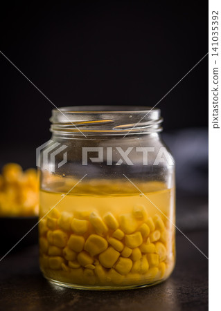 Jar Of Canned Sweet Corn In Brine With Bowl On Dark Kitchen Surface Jar Of Canned Sweet Corn In Brine With Bowl On Dark Kitchen Surface 141035392