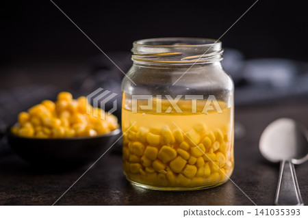 Jar Of Canned Sweet Corn In Brine With Bowl On Dark Kitchen Surface 141035393