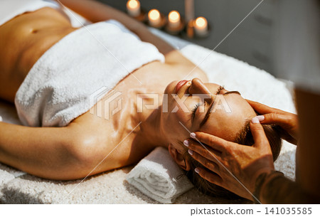 Candlelit Head Massage Close Up Therapist Hands Cradle Womans Face as She Rests Eyes Closed on Spa Table in Warm Glowing Amber Candlelight from Behind Candlelit Head Massage Close Up Therapist Hands Cradle Womans Face as She Rests Eyes Closed on Spa Table in Warm Glowing Amber Candlelight from Behind 141035585