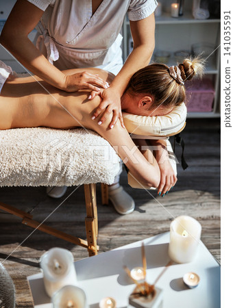 Candlelit Spa Close Up of Therapist Hands Applying Pressure to Womans Upper Back and Shoulder Blade on Soft Plush Massage Table With Candles in Candlelit Spa Close Up of Therapist Hands Applying Pressure to Womans Upper Back and Shoulder Blade on Soft Plush Massage Table With Candles in 141035591