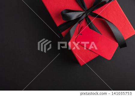 Red gift box with black ribbon and blank tag on dark background Red gift box with black ribbon and blank tag on dark background 141035753