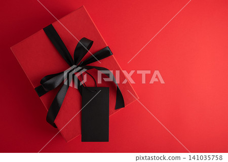 Red gift box with black ribbon and blank tag on red background 141035758