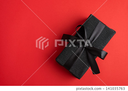 Black gift box creating elegant surprise on red background Black gift box creating elegant surprise on red background 141035763