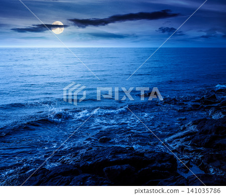 sea coast with stones and rocks at night. summer vacation background. full moon over seascape with rough terrain. fantasy relaxing at the sea. mysterious coast of bulgaria sea coast with stones and rocks at night. summer vacation background. full moon over seascape with rough terrain. fantasy relaxing at the sea. mysterious coast of bulgaria 141035786