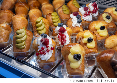 Naples, italy. December 27, 2024. Rows of traditional neapolitan baba rum cakes topped with whipped cream, berries, pistachio, and custard in a bakery display Naples, italy. December 27, 2024. Rows of traditional neapolitan baba rum cakes topped with whipped cream, berries, pistachio, and custard in a bakery display 141035914