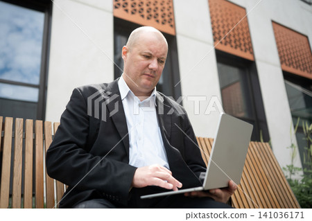 Businessman working on laptop while sitting on bench outdoors 141036171