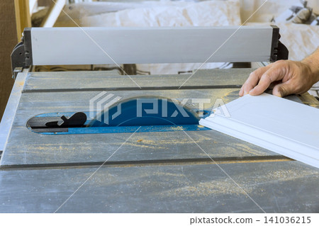 Contractor uses table saw to cut wood for project in workshop with natural light coming in. Contractor uses table saw to cut wood for project in workshop with natural light coming in. 141036215
