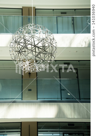 Contemporary spherical chandelier hanging in spacious atrium of luxury office building. Modern lighting design and corporate interior architecture Contemporary spherical chandelier hanging in spacious atrium of luxury office building. Modern lighting design and corporate interior architecture 141036940