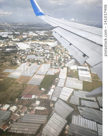 Top-down view of an airplane wing and greenhouses on the ground. Top-down view of an airplane wing and greenhouses on the ground. 141037406