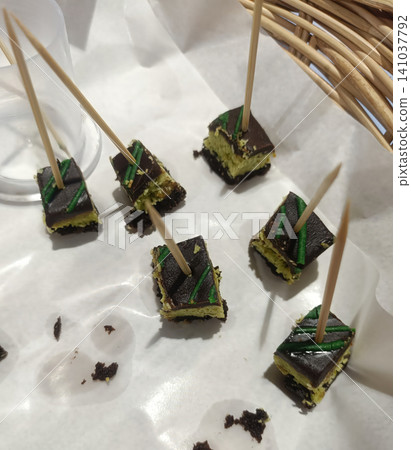 Chocolate cake, skewer, dessert, bite, green icing on white paper party tray Chocolate cake, skewer, dessert, bite, green icing on white paper party tray 141037792