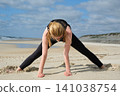 Woman practicing wide leg forward bend yoga pose on a sandy beach, enhancing flexibility, mindfulness, balance, wellness, relaxation, and healthy living 141038754