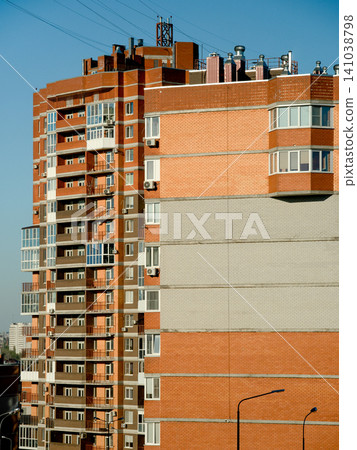 A multi-story residential building with numerous balconies, brick walls, and large windows, illuminated by clear daylight A multi-story residential building with numerous balconies, brick walls, and large windows, illuminated by clear daylight 141038798