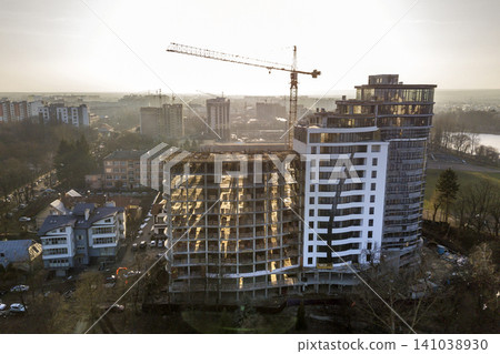 Apartment or office tall building under construction, top view. Tower crane and city landscape stretching to horizon. Drone aerial photography. Apartment or office tall building under construction, top view. Tower crane and city landscape stretching to horizon. Drone aerial photography. 141038930