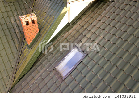 Close-up of new attic plastic window installed in shingled house roof. Professionally done building and construction work, roofing and installation concept. Close-up of new attic plastic window installed in shingled house roof. Professionally done building and construction work, roofing and installation concept. 141038931