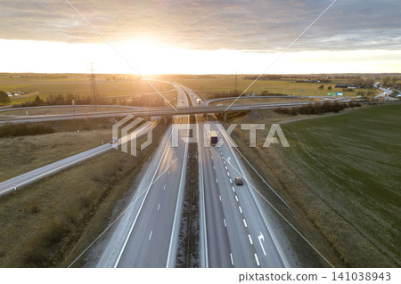 Aerial view of modern highway road intersection at dawn on rural landscape and raising sun background. Drone photography. Aerial view of modern highway road intersection at dawn on rural landscape and raising sun background. Drone photography. 141038943