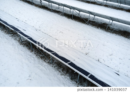 Aerial view of sustainable electrical power plant with solar photovoltaic panels covered with snow in winter for producing clean energy. Concept of low effectivity of renewable electricity in north Aerial view of sustainable electrical power plant with solar photovoltaic panels covered with snow in winter for producing clean energy. Concept of low effectivity of renewable electricity in north 141039037