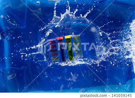 PH acid level test kit on quality water on purple yellow. PH acid level tester kit fall on water splashing splattering over blue background, top angle PH acid level test kit on quality water on purple yellow. PH acid level tester kit fall on water splashing splattering over blue background, top angle 141039145