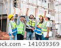Happy Construction Team Raising Hands Together in Celebration at Construction Site 141039369
