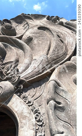 Closeup carved stone gate facade with flowing organic relief under blue sky Closeup carved stone gate facade with flowing organic relief under blue sky 141039390