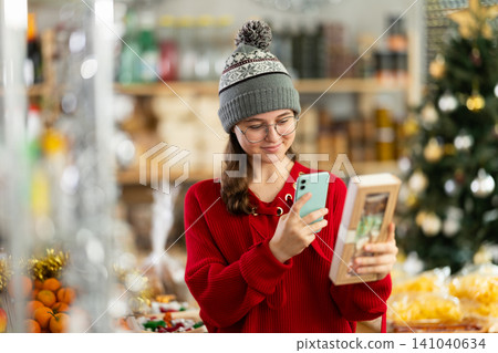European teen girl customer at shop scans QR code on nougat package using phone camera European teen girl customer at shop scans QR code on nougat package using phone camera 141040634