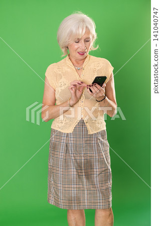Mature woman in beige suit scrolls phone screen, on green screen background Mature woman in beige suit scrolls phone screen, on green screen background 141040747
