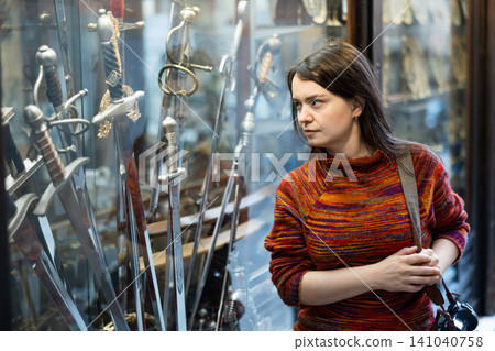 Woman choosing old-fashioned sword in souvenir shop Woman choosing old-fashioned sword in souvenir shop 141040758