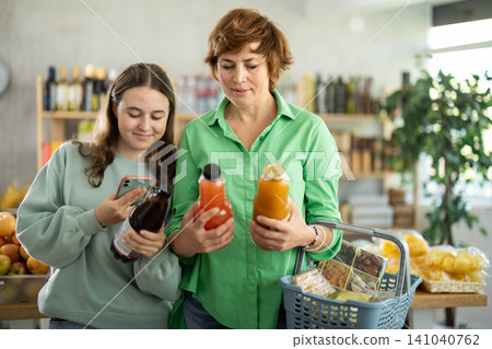 Mother and daughter choose tasty juice together in grocery section of supermarket Mother and daughter choose tasty juice together in grocery section of supermarket 141040762
