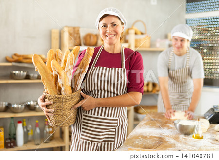 Adult woman baker with basket of baguettes Adult woman baker with basket of baguettes 141040781