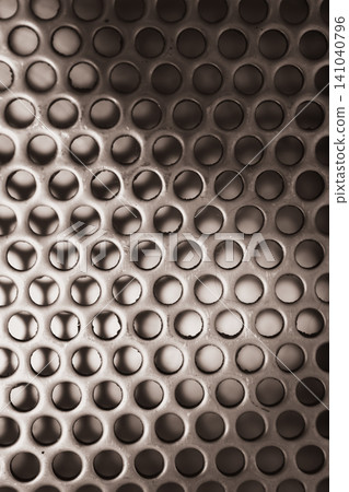 Perforated metal surface creating a textured industrial background, showing a pattern of circular holes and reflecting light with a monotone silver gray aesthetic Perforated metal surface creating a textured industrial background, showing a pattern of circular holes and reflecting light with a monotone silver gray aesthetic 141040796
