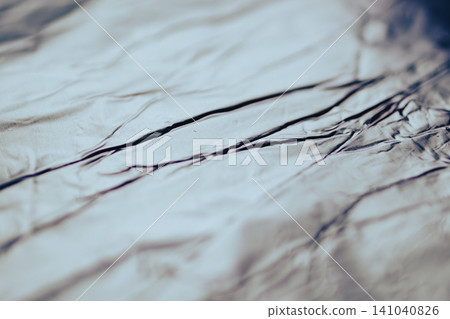 Wrinkled silver foil reflecting light, creating an abstract metallic texture with dynamic creases and shadows, perfect as a background or conceptual element Wrinkled silver foil reflecting light, creating an abstract metallic texture with dynamic creases and shadows, perfect as a background or conceptual element 141040826