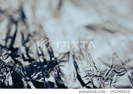 Crumpled aluminum foil forming a textured abstract background, reflecting light and creating a shiny metallic surface with deep shadows and bright areas 141040828
