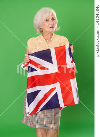 Elderly woman in summer clothes with large flag of UK posing on a green background. Chroma key compositing Elderly woman in summer clothes with large flag of UK posing on a green background. Chroma key compositing 141040846