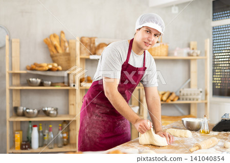 Man works in bakery as baker, kneads dough, works with flour. Man works in bakery as baker, kneads dough, works with flour. 141040854
