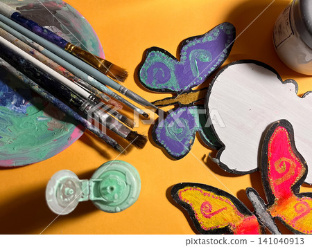 Crafting colorful butterfly shapes with various paintbrushes and acrylic paints on an orange background, symbolizing childhood creativity, art education, and learning activities Crafting colorful butterfly shapes with various paintbrushes and acrylic paints on an orange background, symbolizing childhood creativity, art education, and learning activities 141040913