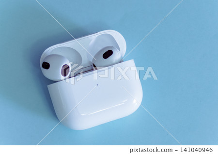 White wireless earbuds in an open charging case sitting on a light blue background, representing modern education technology, remote working, and personal entertainment White wireless earbuds in an open charging case sitting on a light blue background, representing modern education technology, remote working, and personal entertainment 141040946