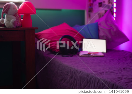 Teenager bedroom showing modern aesthetic with purple neon lighting, tablet, headphones on a bed and cozy pillows inside a contemporary interior styled for youth Teenager bedroom showing modern aesthetic with purple neon lighting, tablet, headphones on a bed and cozy pillows inside a contemporary interior styled for youth 141041099