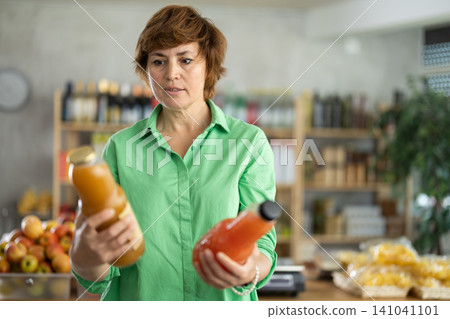 Grocery shopping at supermarket - woman chooses juice, tomato, grapefruit or peach Grocery shopping at supermarket - woman chooses juice, tomato, grapefruit or peach 141041101