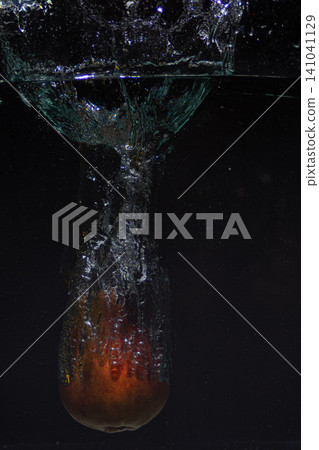 Vertical side view of a fresh red apple splashing into refreshing clear water creating bubbles 141041129