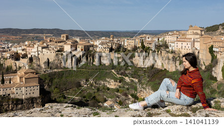 Woman sitting on rock over cityscape of Cuenca, Spain Woman sitting on rock over cityscape of Cuenca, Spain 141041139