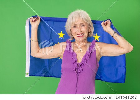 Mature woman in summer clothes with large flag of European Union posing on a green background. Chroma key compositing Mature woman in summer clothes with large flag of European Union posing on a green background. Chroma key compositing 141041208