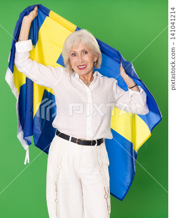 Elderly woman in white clothes with large flag of Sweden posing on green background. Chroma key compositing Elderly woman in white clothes with large flag of Sweden posing on green background. Chroma key compositing 141041214