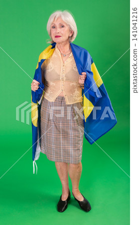 Positive senior woman in beige suit holds big national flag of Sweden, green background Positive senior woman in beige suit holds big national flag of Sweden, green background 141041216