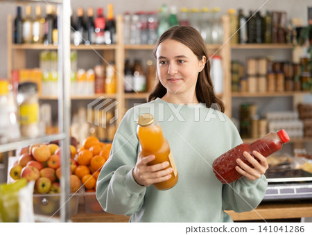 Teen girl hold packages bottles and choose consider juice in store Teen girl hold packages bottles and choose consider juice in store 141041286